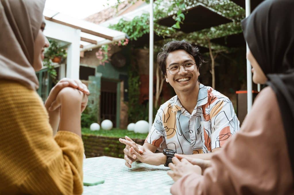 three peopel sitting at a table in in outdoor courtyard depicting the vibrant lifestyle at Flora apartments in summerville sc - AdobeStock 354630738