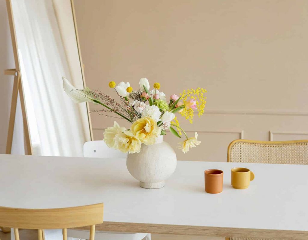 White table with a floral arrangement in the center with a long mirror in the corner of the room depicting the vibrant lifestyle at Flora apartments in summerville sc - marina podrez l62 amh QEs unsplash