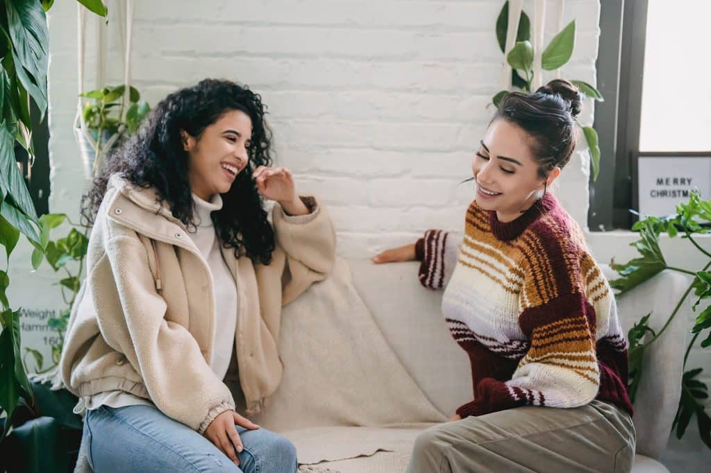 two people sitting on a loveseat laughing depicting the vibrant lifestyle at Flora apartments in summerville sc - pexels julia larson 6113422